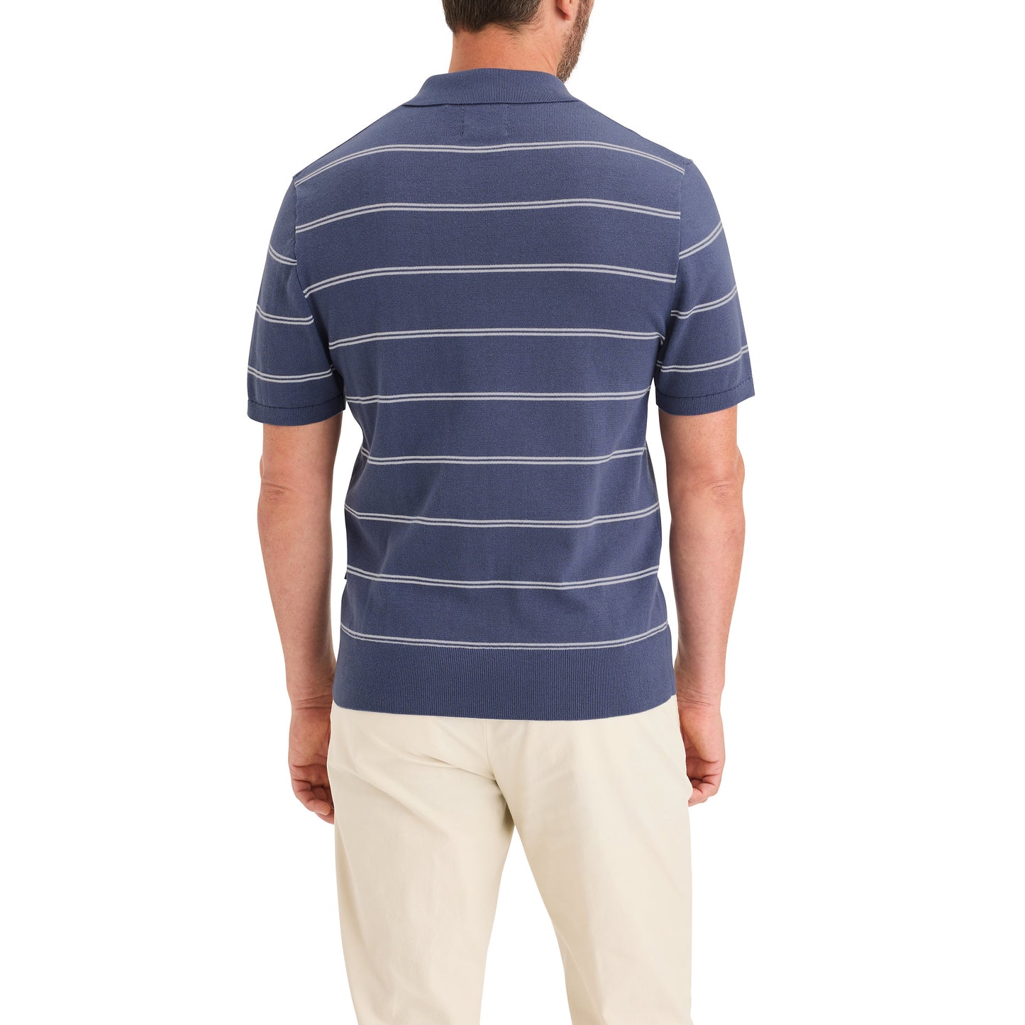 A man stands facing away, wearing the Dockers Men's Sweater Polo—a blue, short-sleeve, collared shirt with white horizontal stripes made from BCI Cotton—and beige pants.