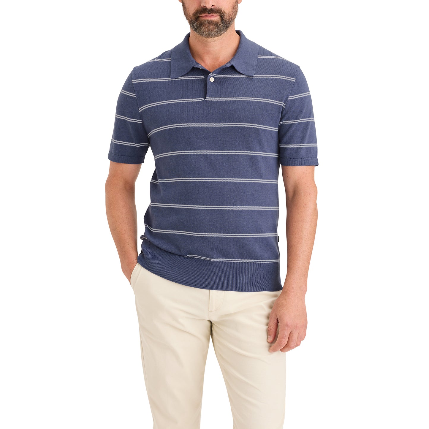 A man wears a Dockers Men's Sweater Polo with blue and white horizontal stripes, crafted from BCI Cotton, paired with beige pants and stands with one hand in his pocket.