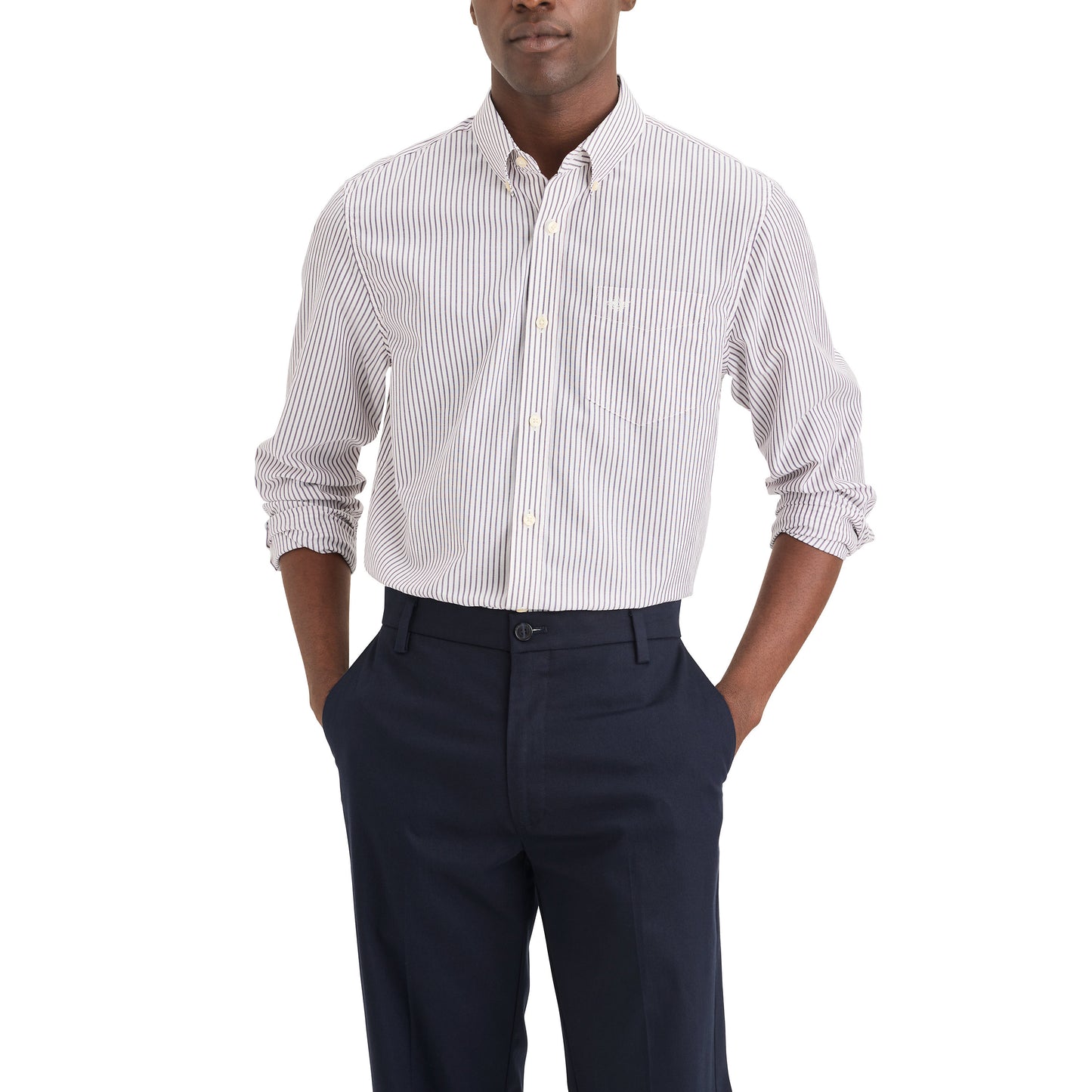 A man wearing the Dockers Men's Signature Shirt, LS—a white button-up with thin black stripes—and dark navy dress pants, stands with his hands in his pockets.