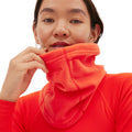 The person in vibrant orange clothing adjusts their Halfdays Marquis Fleece Neck Warmer for a snug fit.