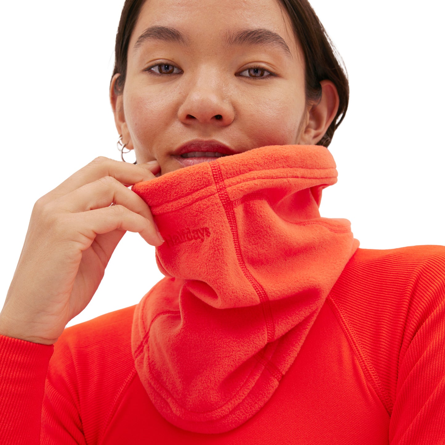 The person in vibrant orange clothing adjusts their Halfdays Marquis Fleece Neck Warmer for a snug fit.