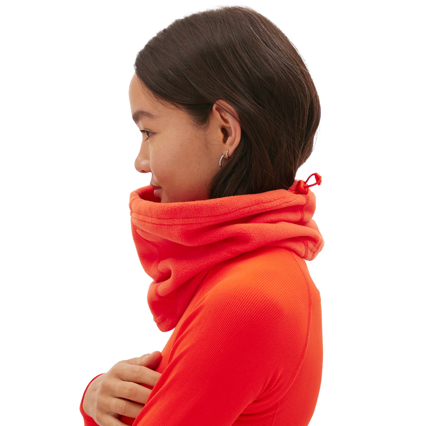 A person in profile wears a bright orange turtleneck, scarf, and the Marquis Fleece Neck Warmer by Halfdays, with arms crossed against a plain white background.
