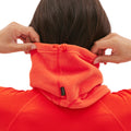 A person adjusts the hood of an orange Halfdays Marquis Fleece Neck Warmer, ensuring it fits snugly from the back view.