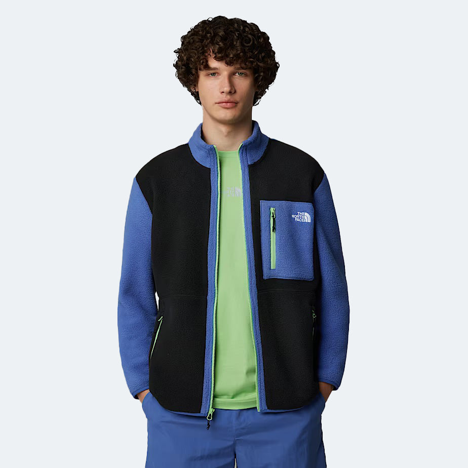 Against a light background, a person wears The North Face M Yumiori Full Zip jacket in blue and black for reliable warmth. A green shirt is visible beneath the cozy midweight fleece.