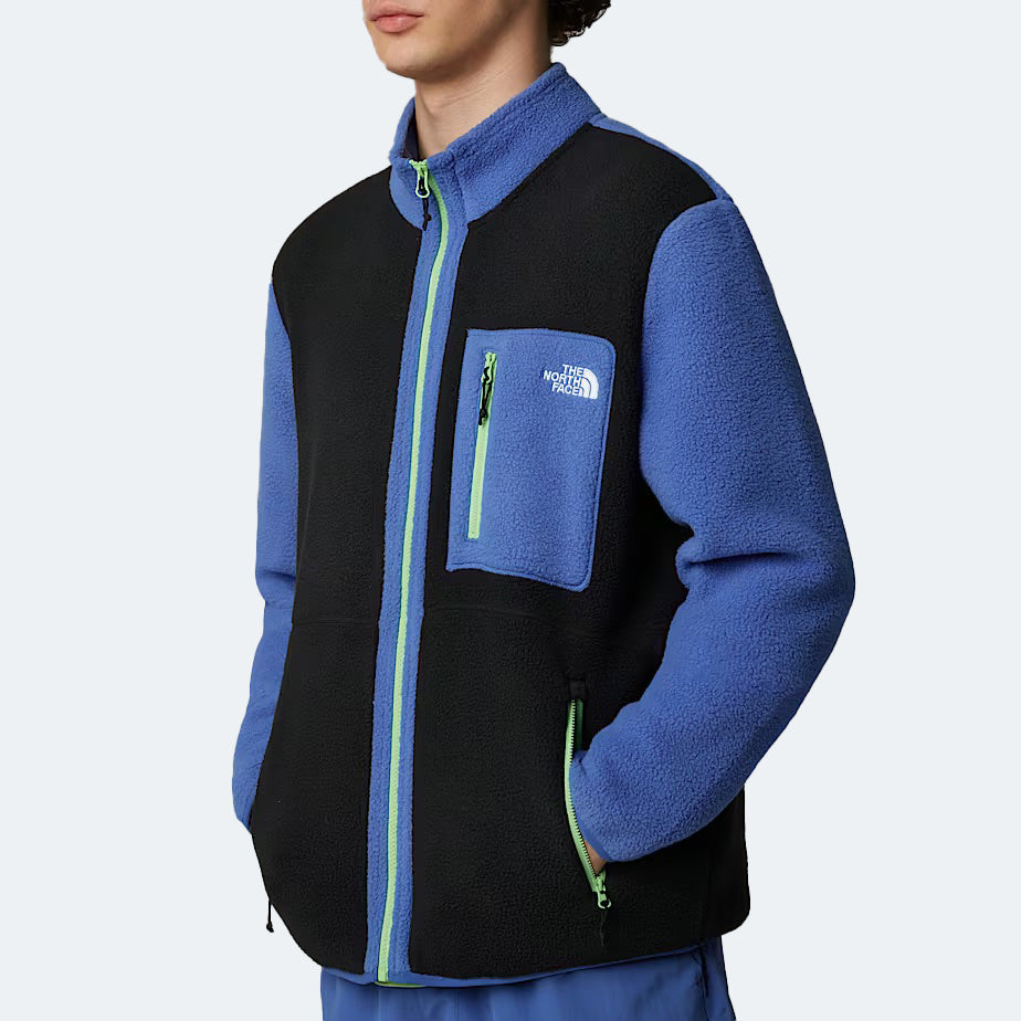 Against a light background, a person wears The North Face M Yumiori Full Zip jacket in blue and black. Green zippers add a pop of color while its midweight fleece keeps you warm on chilly days.