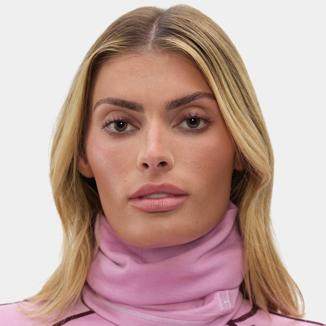 Woman wearing a pink gaiter and matching top with a plain background