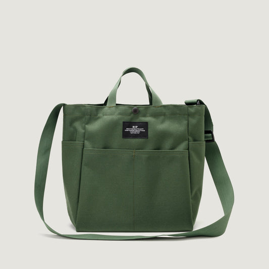 Green canvas Multi Pocket Bag Medium tote bag with a front pocket and adjustable strap, featuring a black Bags in Progress label near the top center.