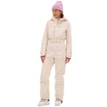 Wearing the vintage racing-style Murphy Ski Suit by Halfdays in light pink, accessorized with a matching beanie and white boots, a person stands gracefully while gazing to the side.
