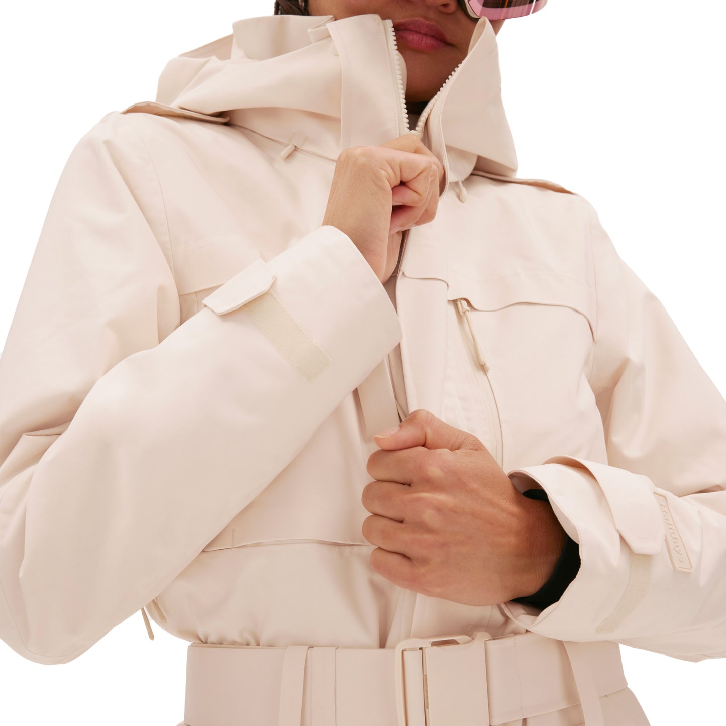 Person zipping up the Murphy Ski Suit from Halfdays, a light-colored, hooded design with a belt that exudes a vintage racing-style vibe.