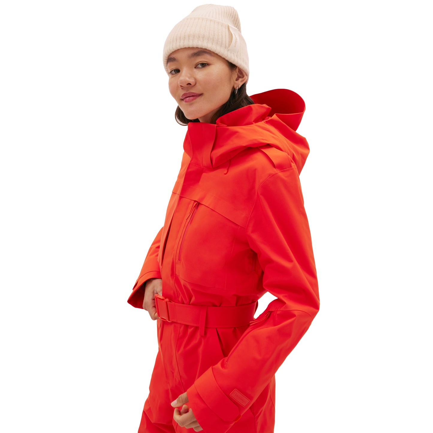 A person is wearing the Murphy Ski Suit by Halfdays, featuring a bright red vintage racing-style jacket with a hood, and a white beanie, standing against a plain white background.