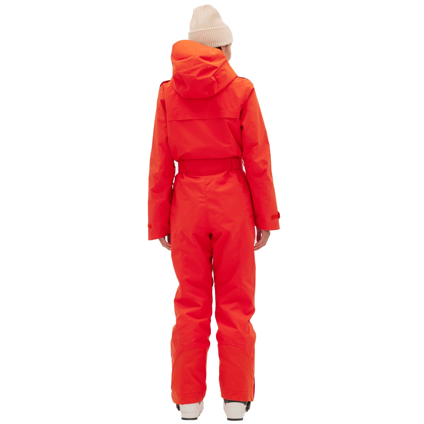 A person dressed in a vintage racing-style Murphy Ski Suit by Halfdays, featuring an orange one-piece design, and a beige beanie stands against a plain white background.