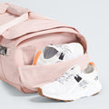 The North Face Base Camp Voyager Duffel - 42L in pink, with its lightweight build and side compartment, is partially open to display white sneakers with orange accents—ideal for stylish, organized travel.