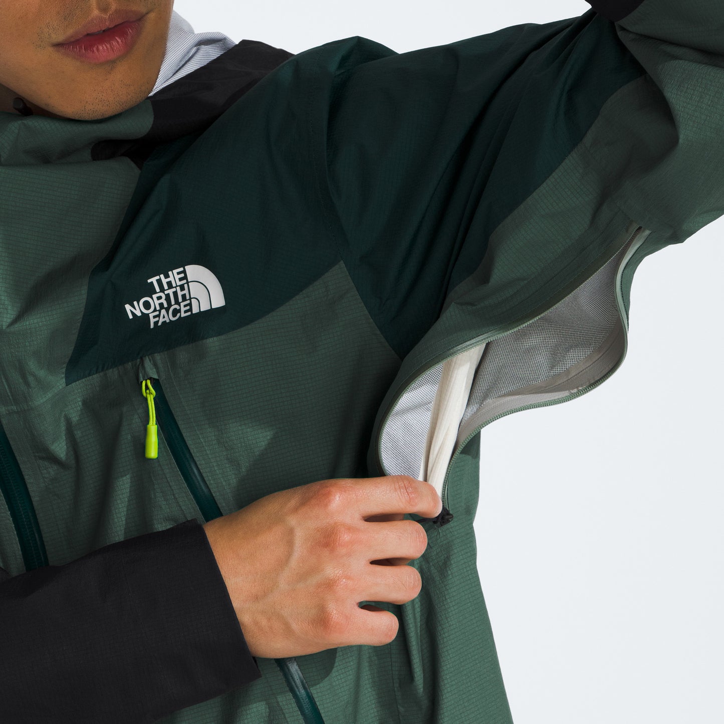 The person adjusts the underarm ventilation zipper of their dark green M Signal 2.5L DryVent jacket, proudly displaying The North Face logo.