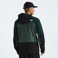 A person wearing a black and green M Signal 2.5L DryVent hooded jacket by The North Face and a black cap, facing away from the camera, with the logo visible on the back of the jacket.