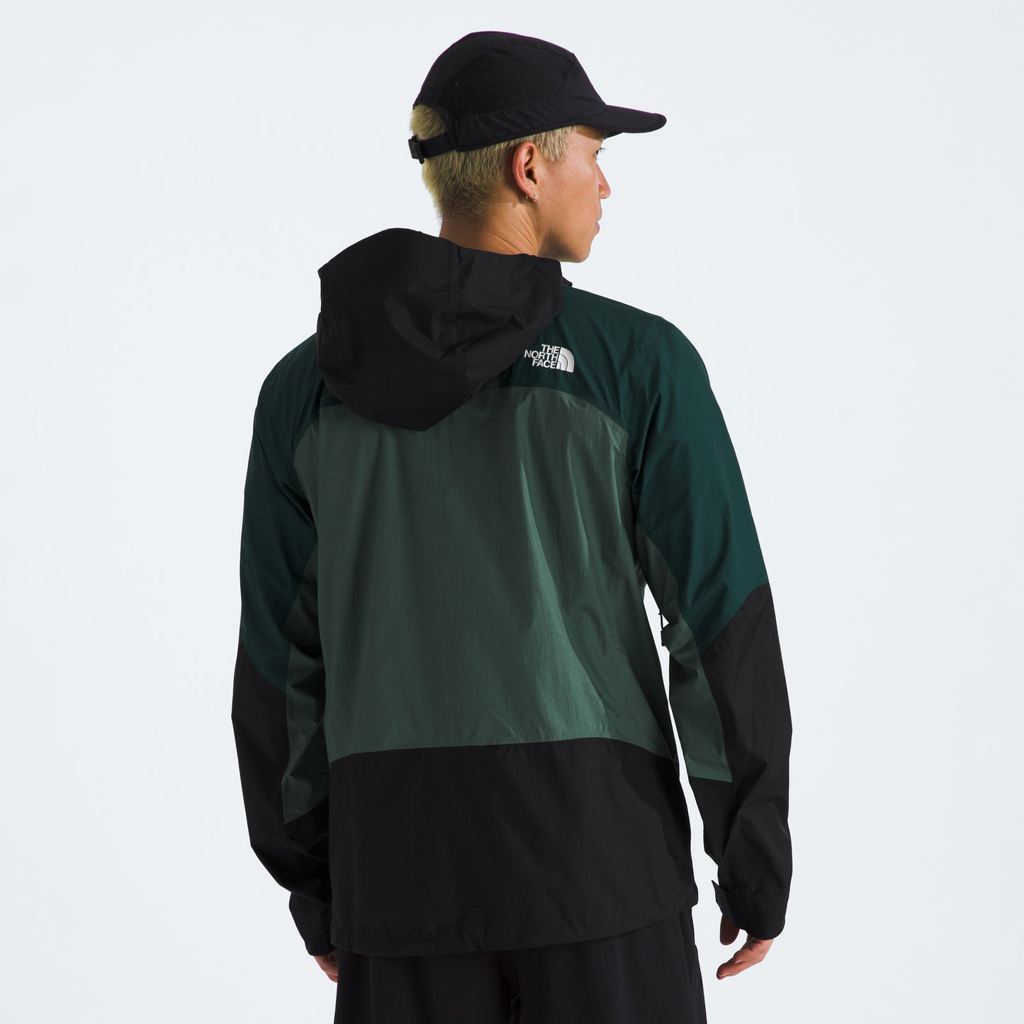 A person wearing a black and green M Signal 2.5L DryVent hooded jacket by The North Face and a black cap, facing away from the camera, with the logo visible on the back of the jacket.