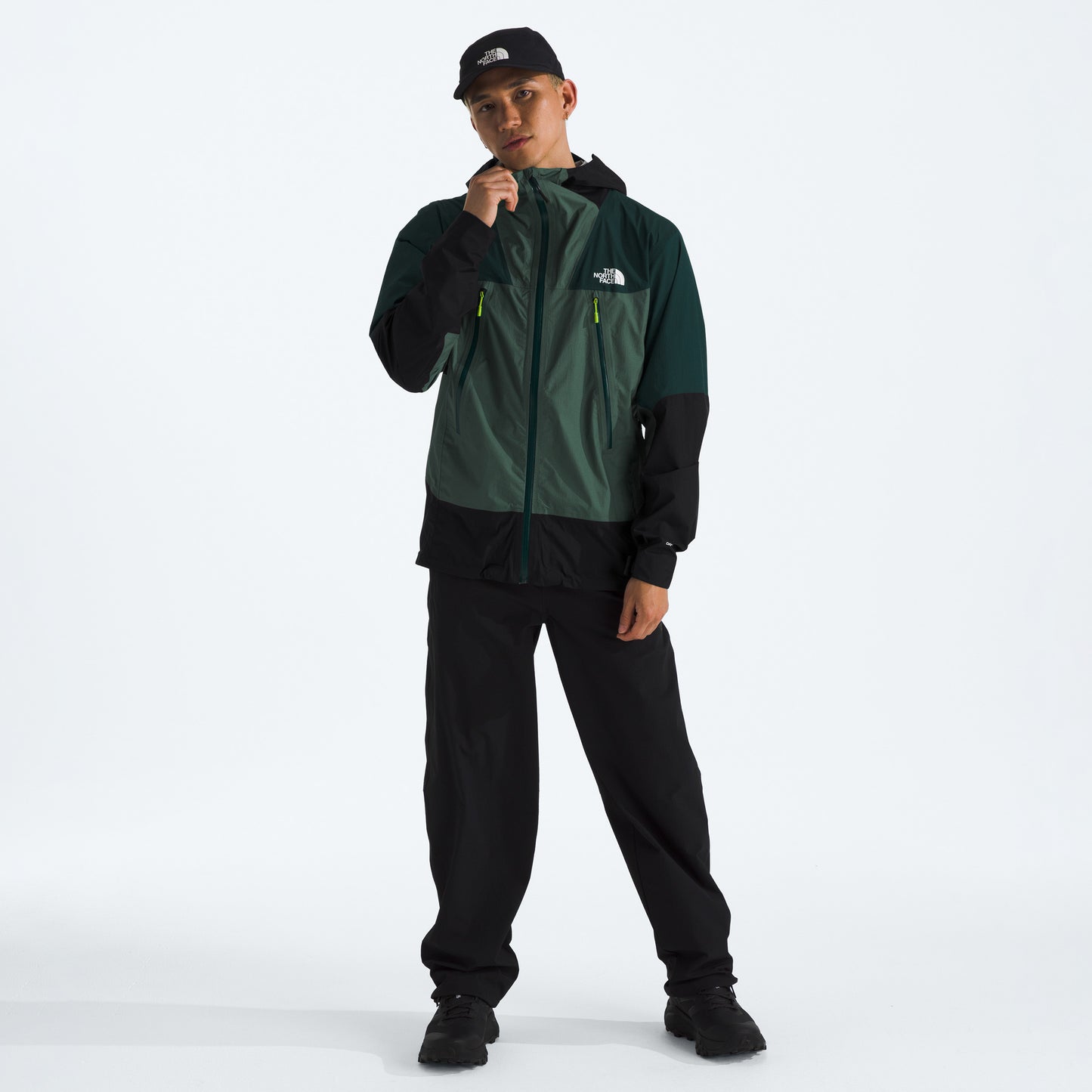 Person wearing The North Face M Signal 2.5L DryVent jacket in green and black, black pants, and a black cap stands against a plain white background.