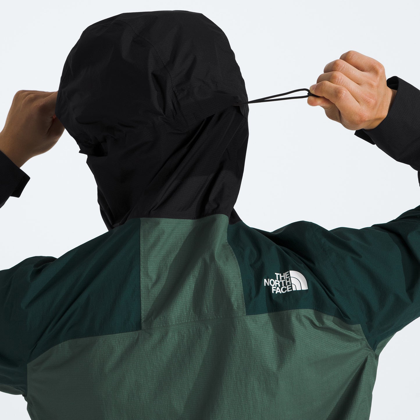 Person adjusts the hood of their black and green M Signal 2.5L DryVent jacket from The North Face, pulling on the drawstring at the back.