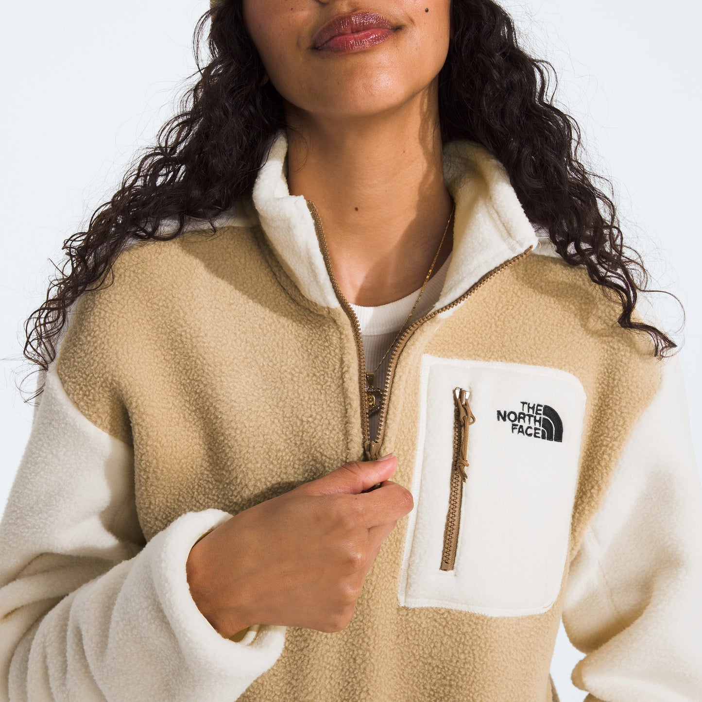 A person wearing The North Face W Yumiori 1/4 Zip fleece jacket in beige and white, made from recycled materials, featuring a chest pocket logo.
