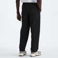 Rear view of a person wearing The North Face M North Dome Wind Pant in black and white sneakers, standing with one hand in a pocket against a plain background.