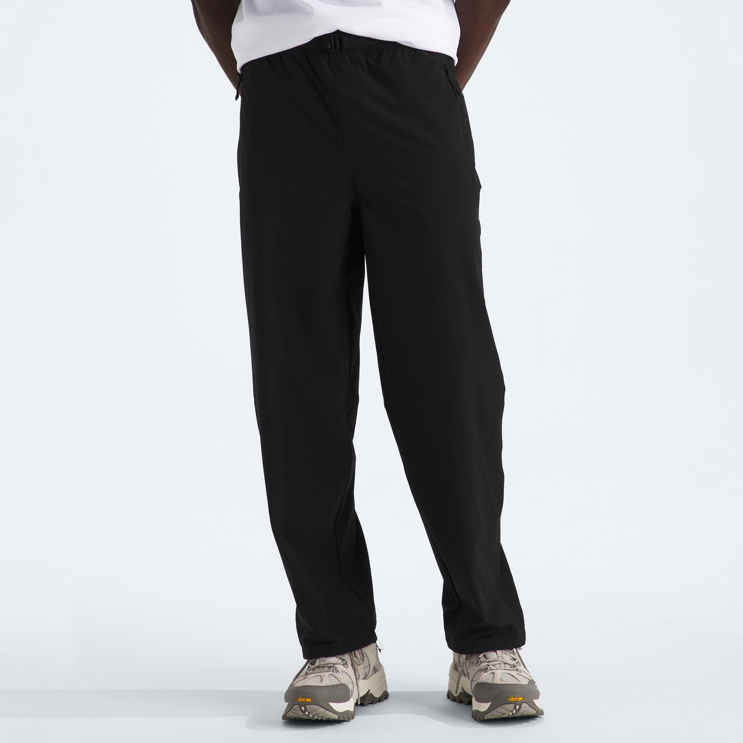 Someone is standing against a plain white background, wearing M North Dome Wind Pant by The North Face in black and paired with white sneakers. Their upper body is not visible.