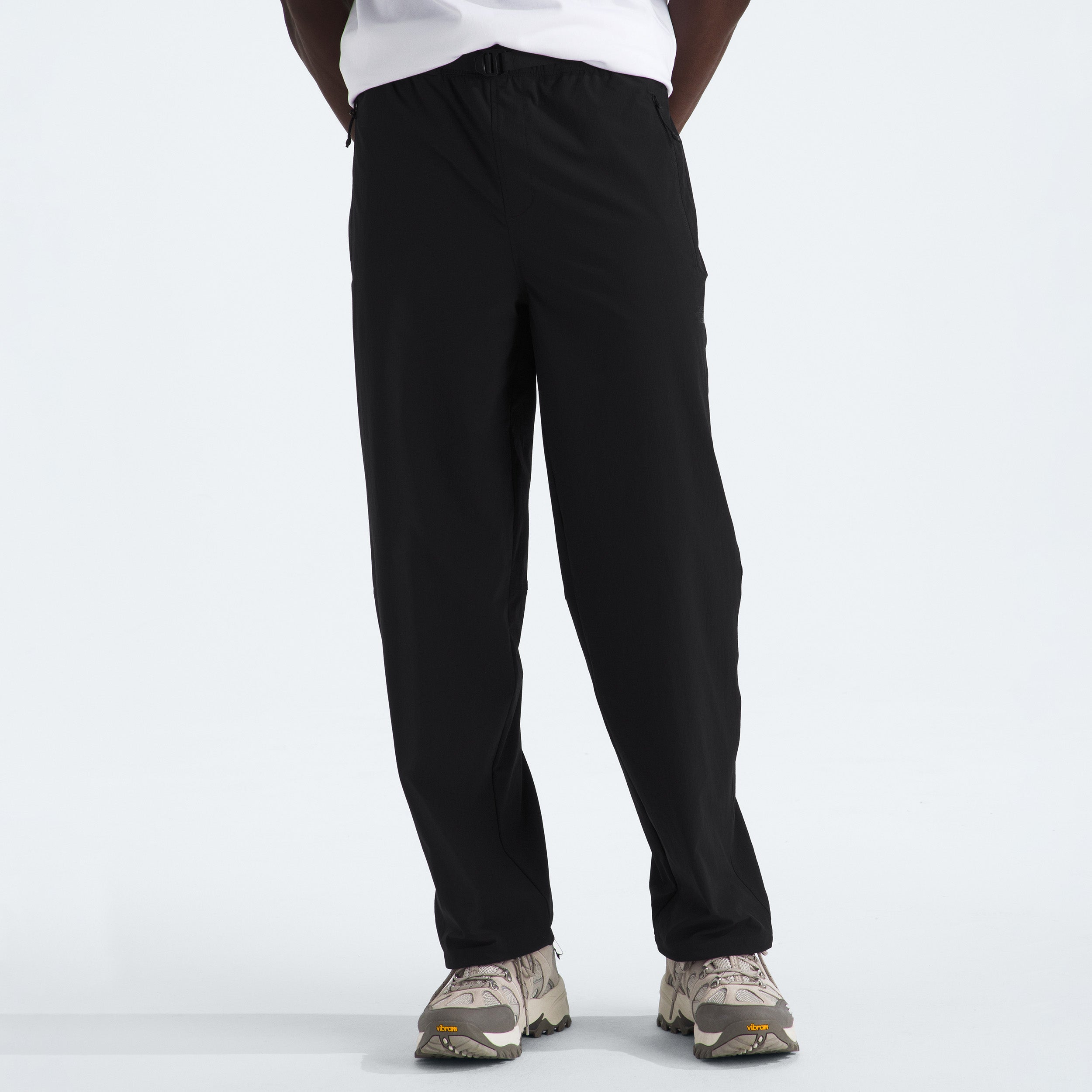 Someone is standing against a plain white background, wearing M North Dome Wind Pant by The North Face in black and paired with white sneakers. Their upper body is not visible.