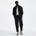A person stands against a plain white background wearing a black jacket, white shirt, The North Face sneakers, sunglasses, a cap, and the M North Dome Wind Pant by The North Face.