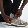 A person adjusts the drawstring hem of The North Face M North Dome Wind Pant, paired with light gray The North Face sneakers and white socks.