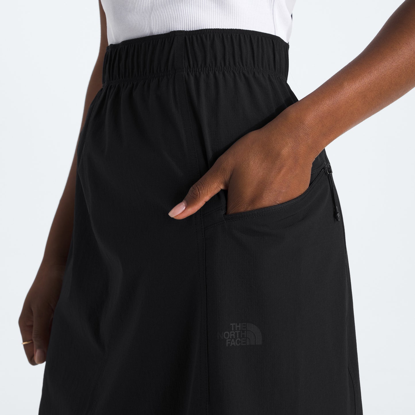 Person wearing a W North Dome Wind Skirt from The North Face in black, with a hand in the pocket, and a white sleeveless top.