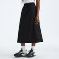 A person in a white top and The North Face W North Dome Wind Skirt with black sneakers and white socks is set against a plain backdrop.