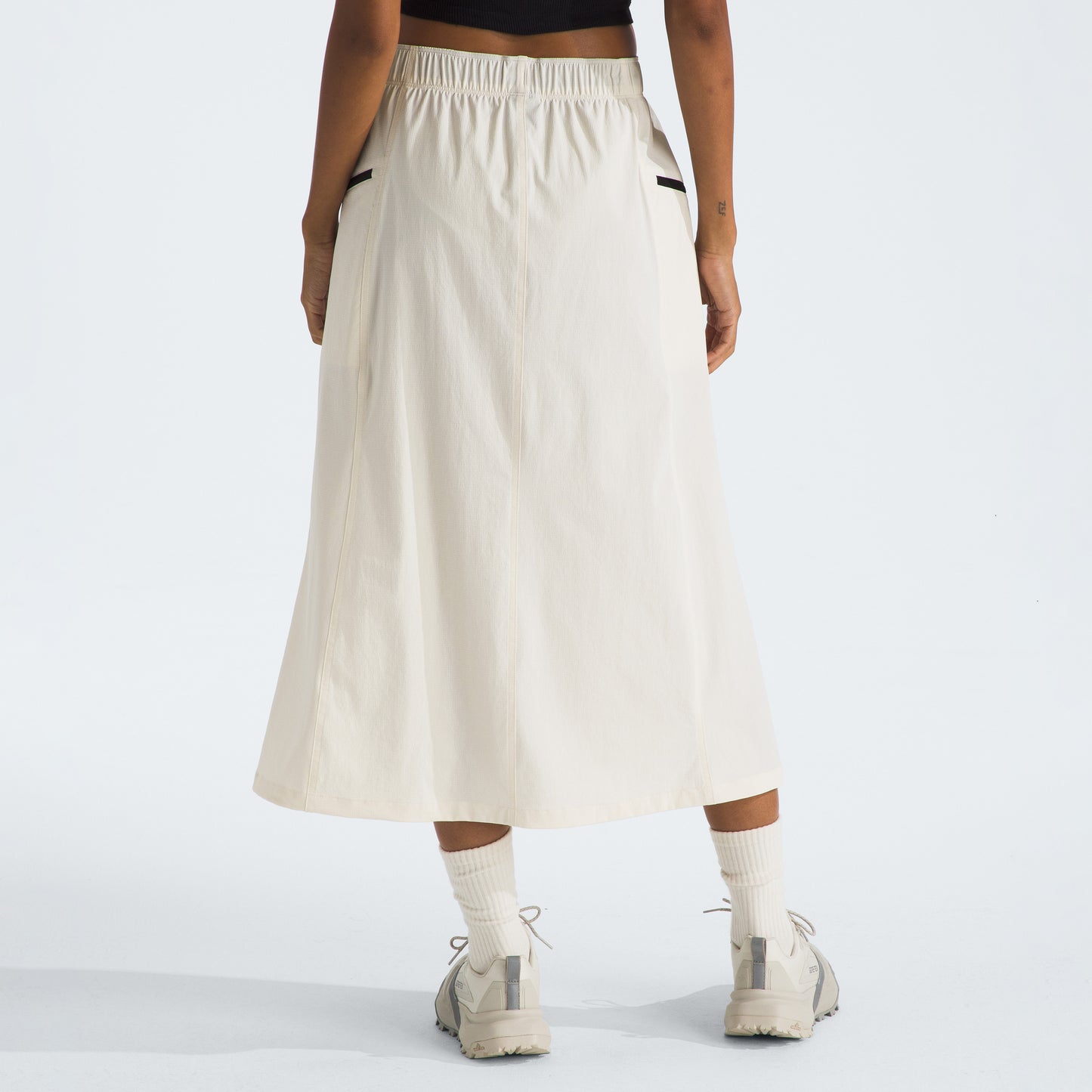 An individual wearing The North Face W North Dome Wind Skirt and sneakers stands with hands at their sides, facing away.