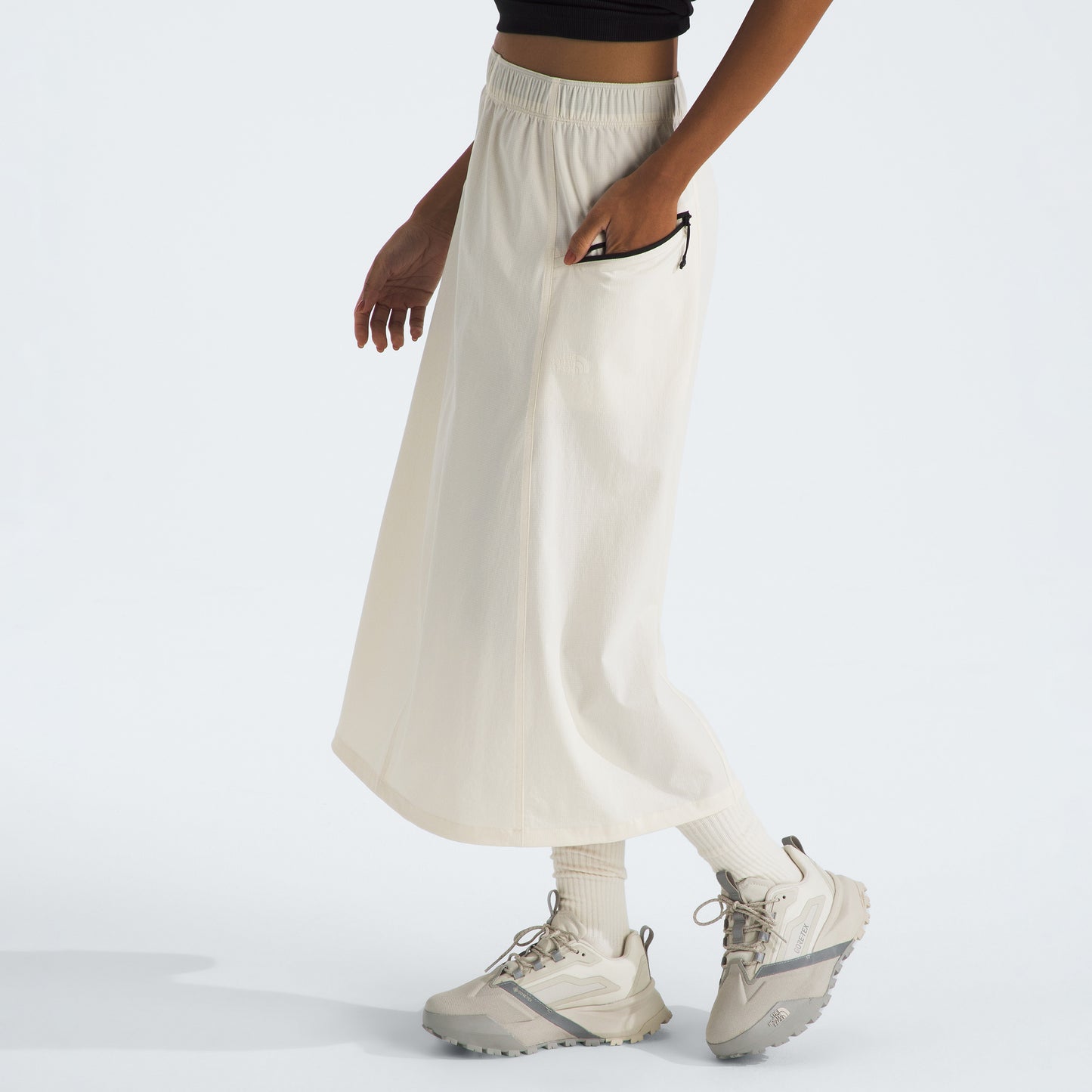A person wearing The North Face W North Dome Wind Skirt, beige sneakers, and a black top stands against a plain background.