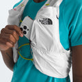 A person in a blue shirt slips their iPhone into the pocket of a white U Summit Run Vest 5 by The North Face, ready for race day.