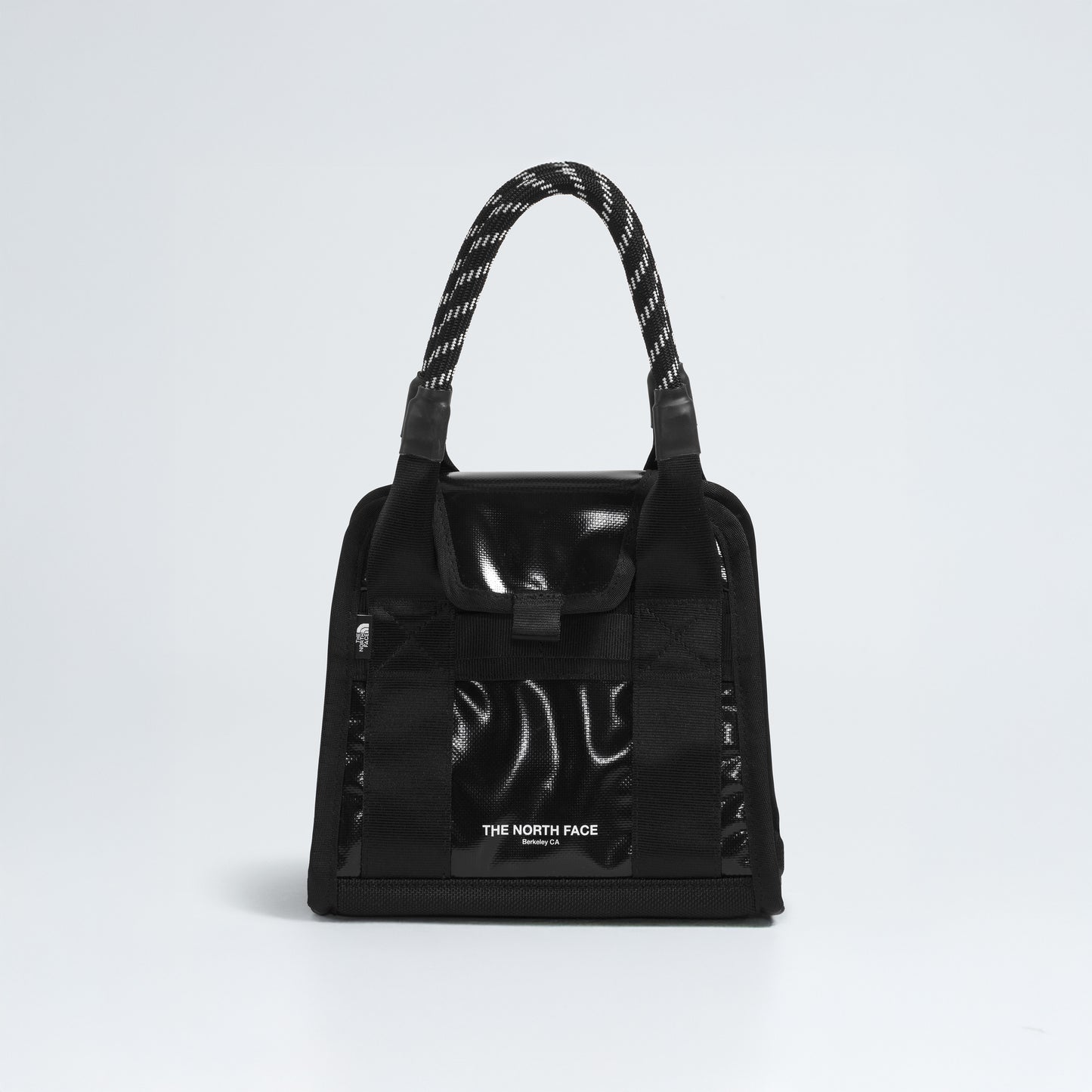 The Base Camp Mini Tote by The North Face, made from recycled fabric, features a black glossy finish, patterned handles, and the iconic logo on a plain white background.
