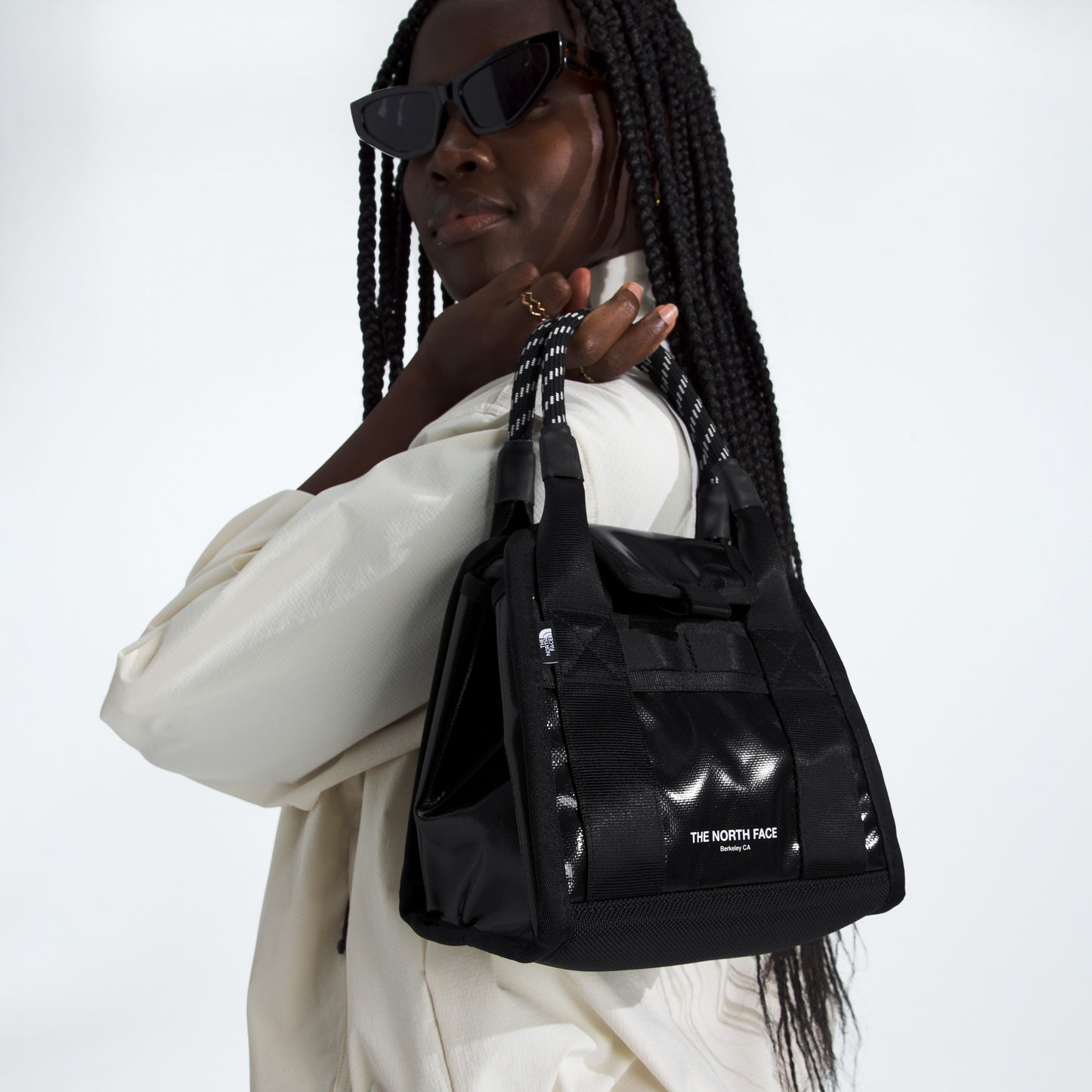 A person wearing sunglasses and a light jacket carries a Base Camp Mini Tote by The North Face, expertly crafted from recycled fabric, over their shoulder.