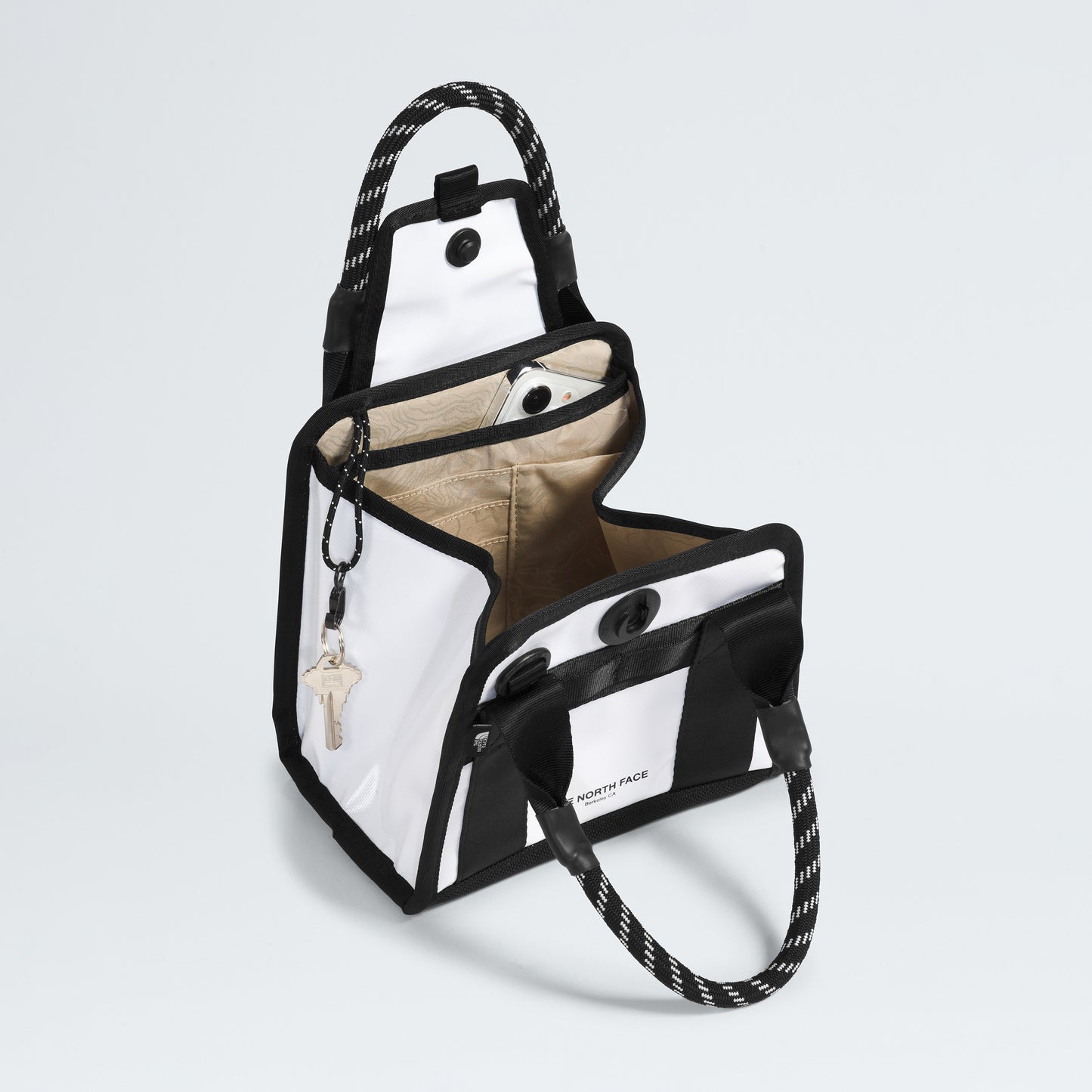 The North Face Base Camp Mini Tote, made from recycled fabric, features a stylish black and white exterior with rope handles. Inside, it has a beige lining and organized compartments, including conveniently clipped keys.