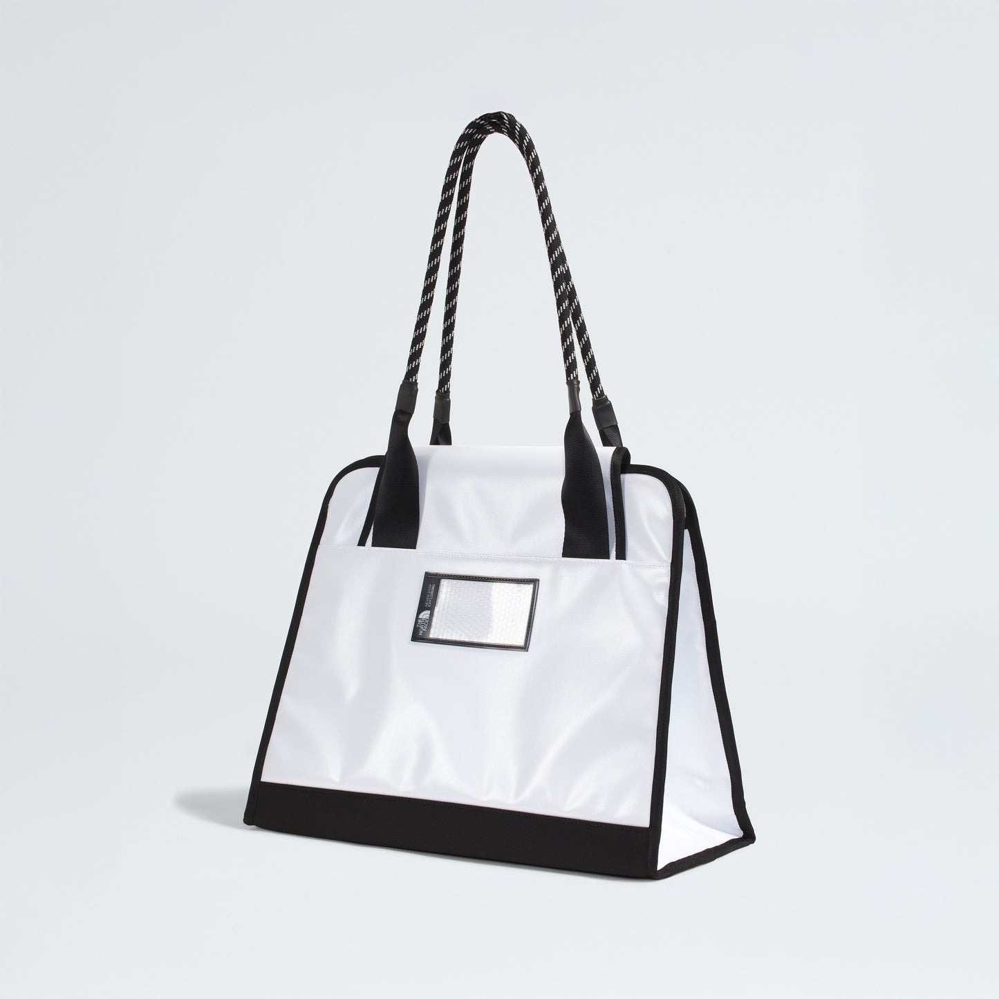 The North Face Base Camp Tote Bag is durable and white, featuring black handles, black trim, a small transparent front pocket for organization—shown against a plain light background.