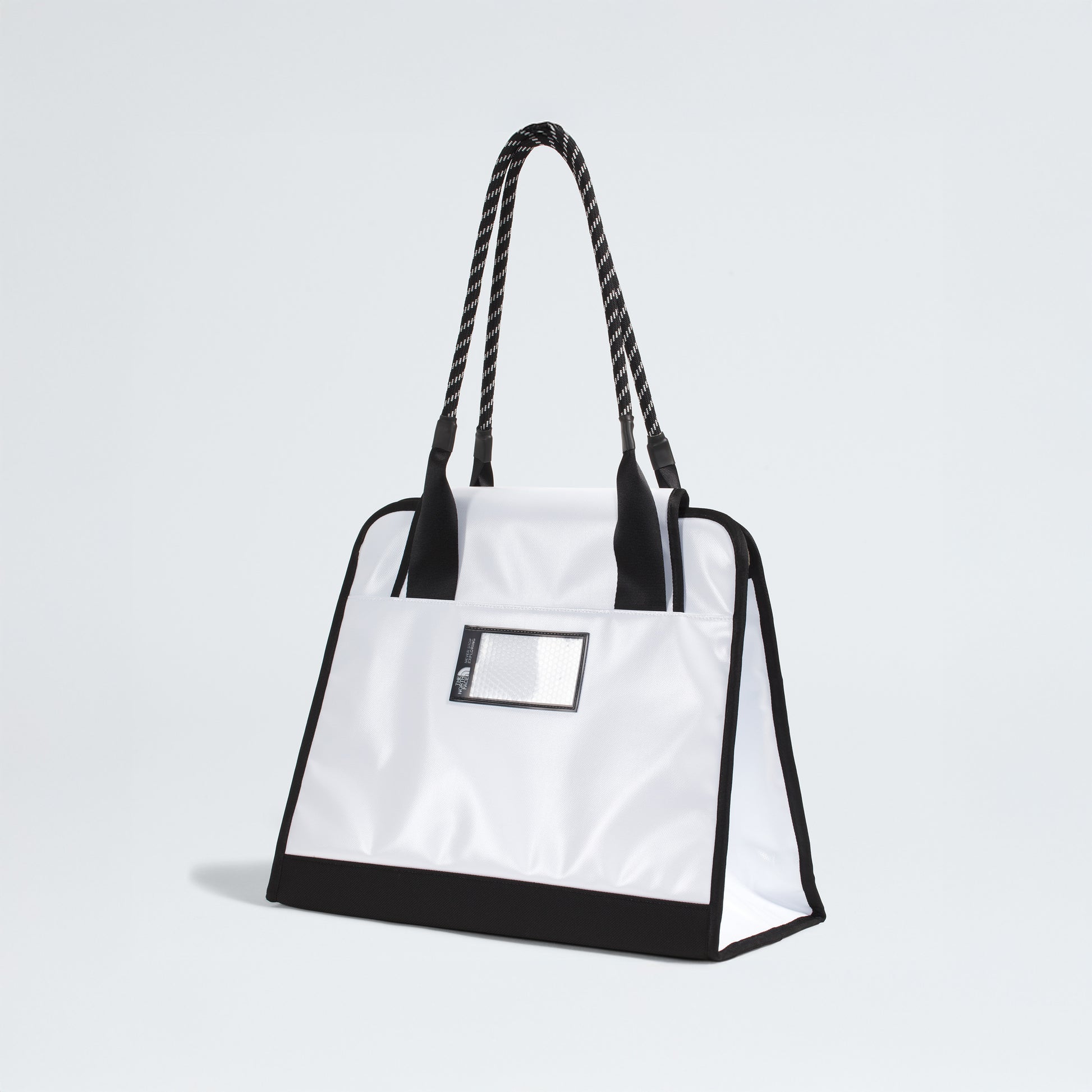 The North Face Base Camp Tote Bag is durable and white, featuring black handles, black trim, a small transparent front pocket for organization—shown against a plain light background.