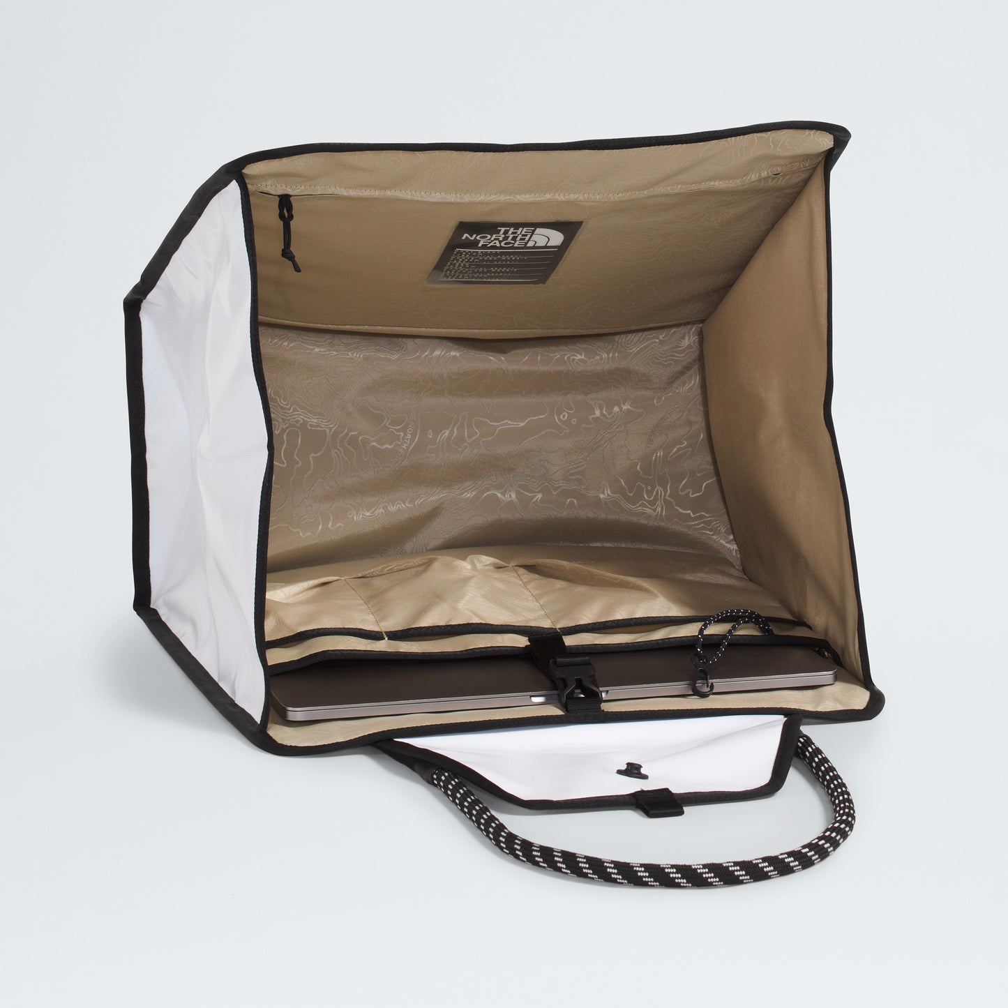 The North Face Base Camp Tote Bag in beige and white features a zippered top, internal pockets, cord, map-patterned lining, and a durable black-and-white woven handle for style and organization.