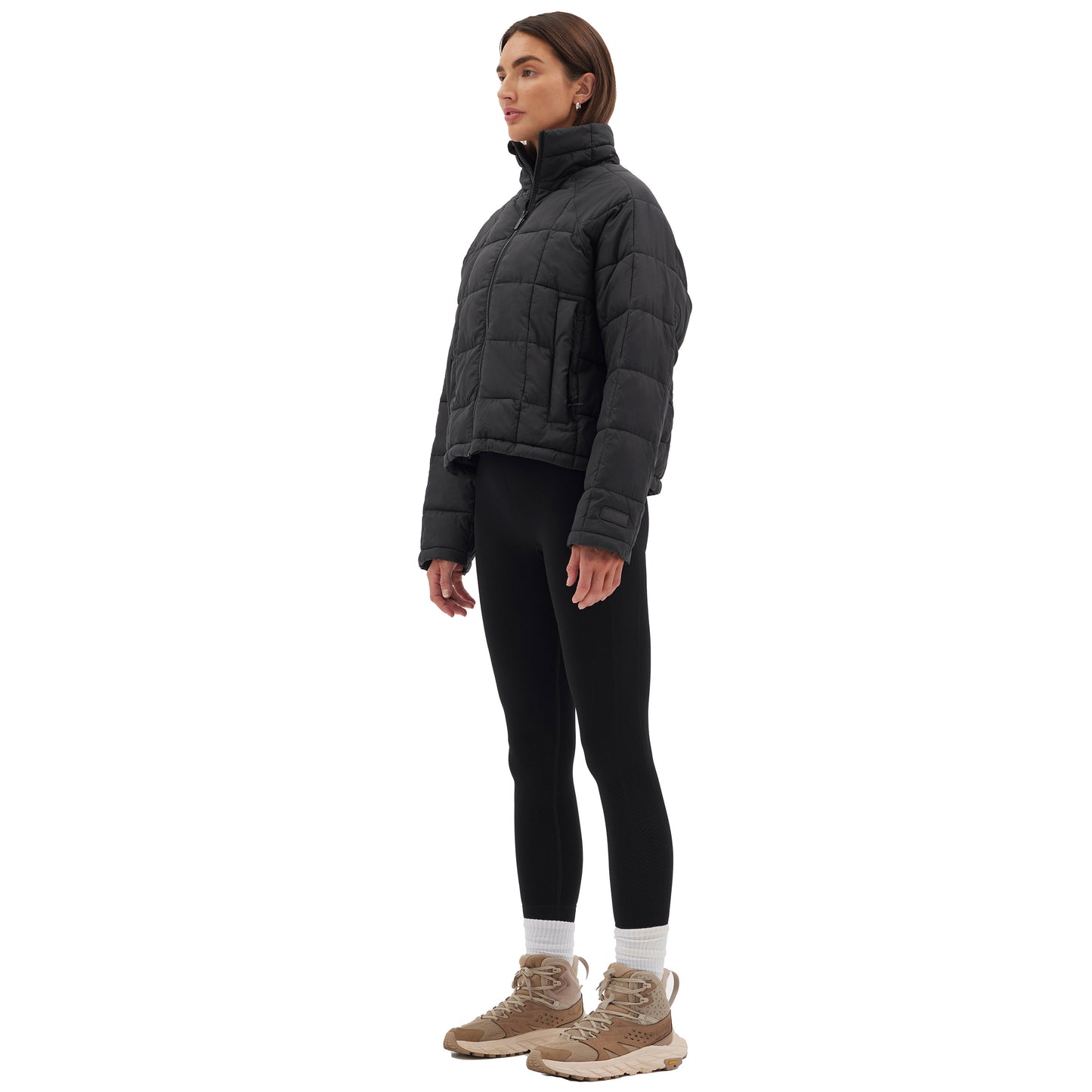 A person wearing the Nellie Packable Puffer Jacket by Halfdays, black leggings, and beige sneakers stands in a side profile against a white background, ready for their next outdoor adventure.