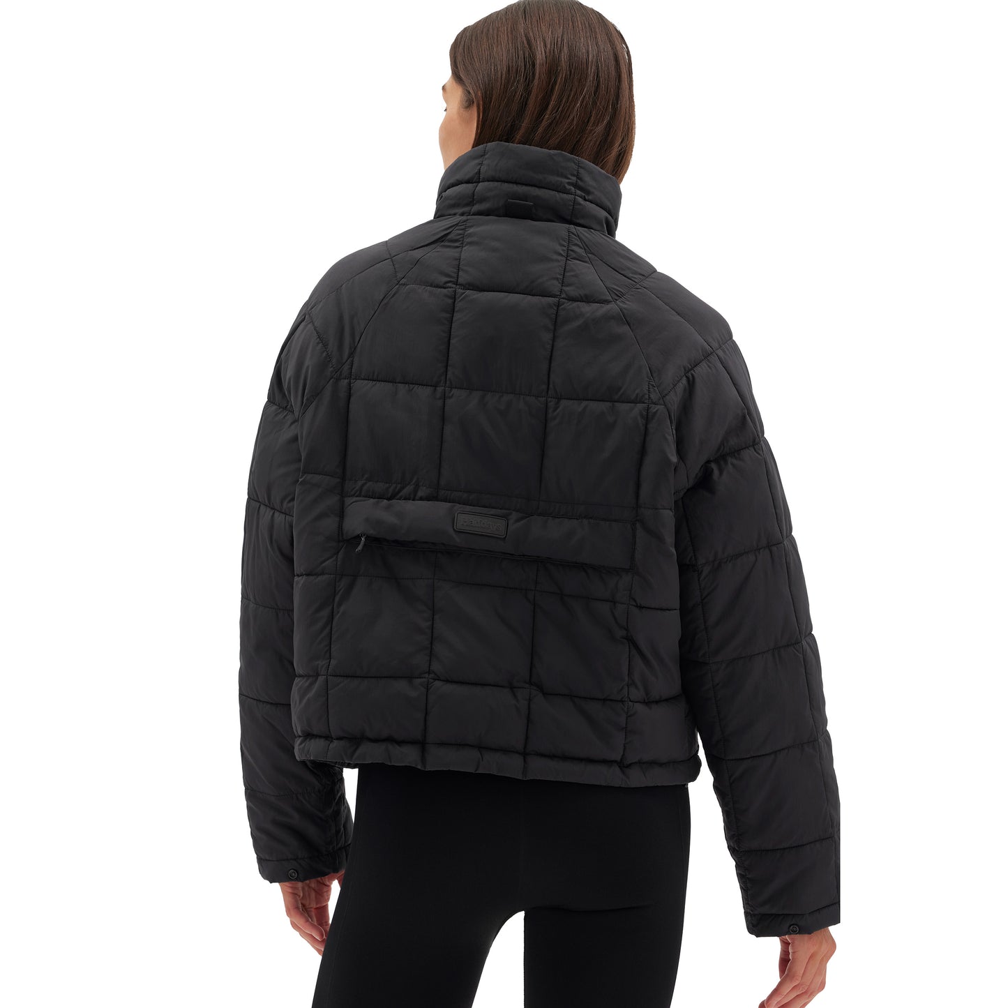 Wearing the Nellie Packable Puffer Jacket by Halfdays and black pants, a person faces away from the camera, perfectly attired for an outdoor adventure.