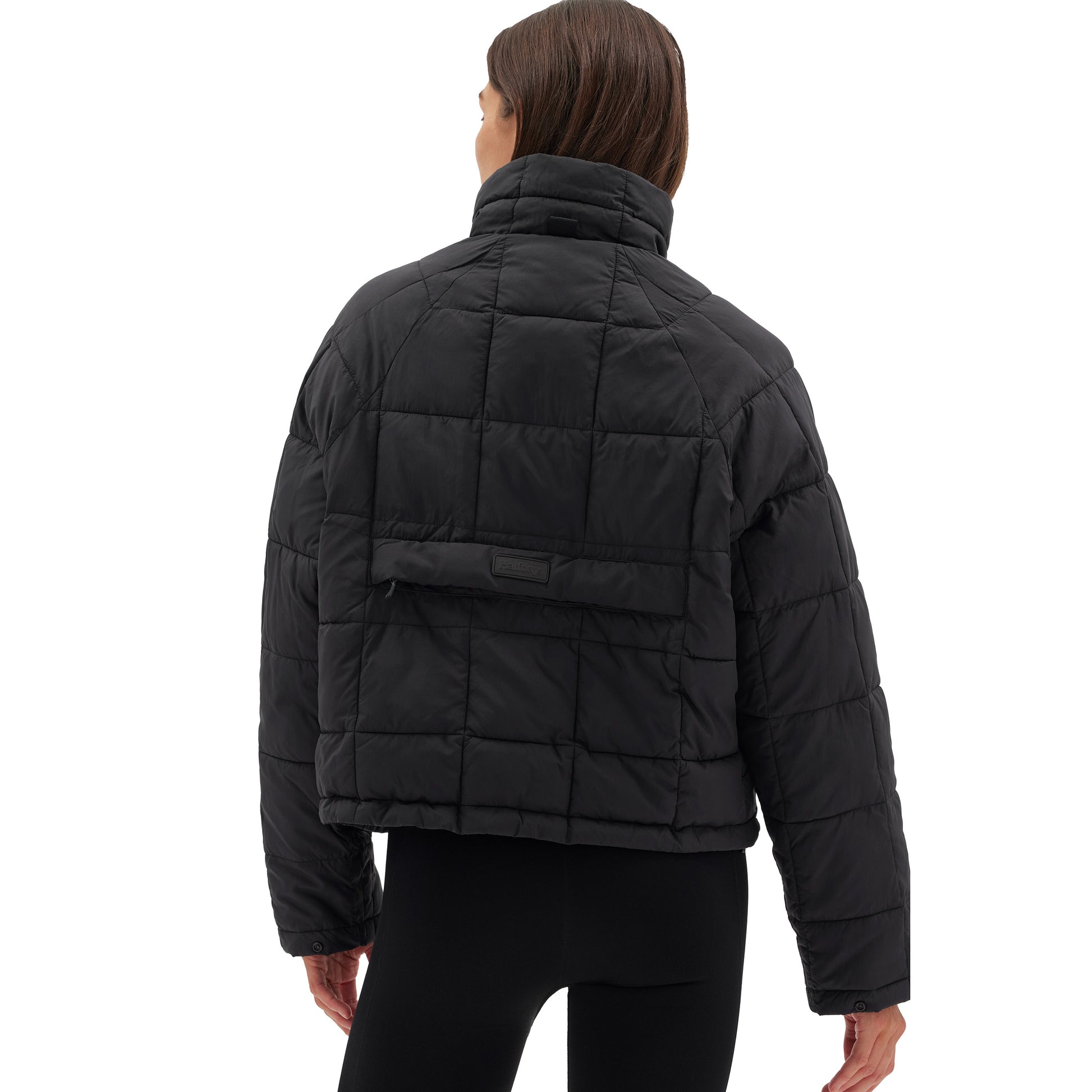 Wearing the Nellie Packable Puffer Jacket by Halfdays and black pants, a person faces away from the camera, perfectly attired for an outdoor adventure.