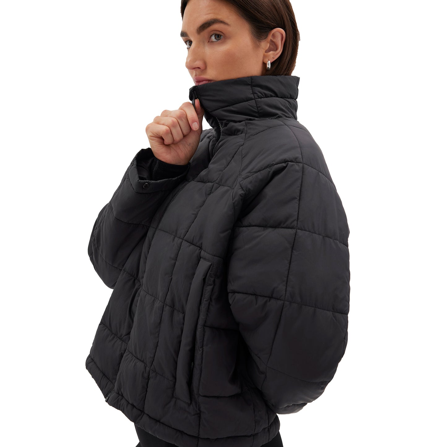 A person wearing the Nellie Packable Puffer Jacket by Halfdays is turned to the side with one hand raised to their neck, ready for an outdoor adventure.