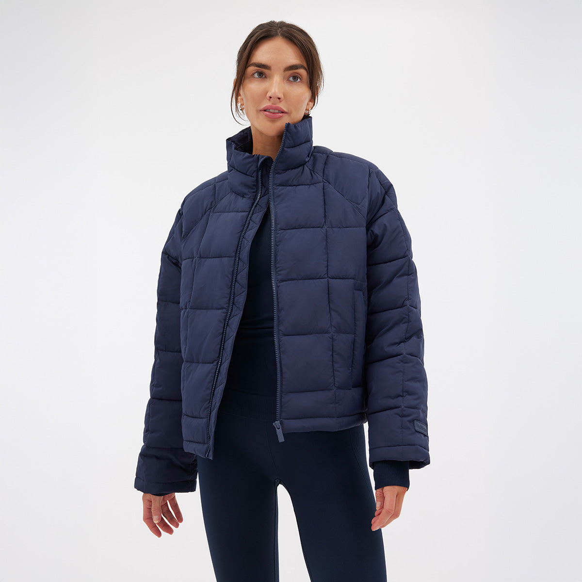 A person stands against a white background wearing Halfdays' Nellie Packable Puffer Jacket in navy, complemented by navy pants, and looks directly at the camera, embodying readiness for outdoor adventure.