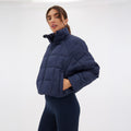 Wearing the Nellie Packable Puffer Jacket by Halfdays and dark leggings, a person stands against a plain white background, prepared for any outdoor adventure.