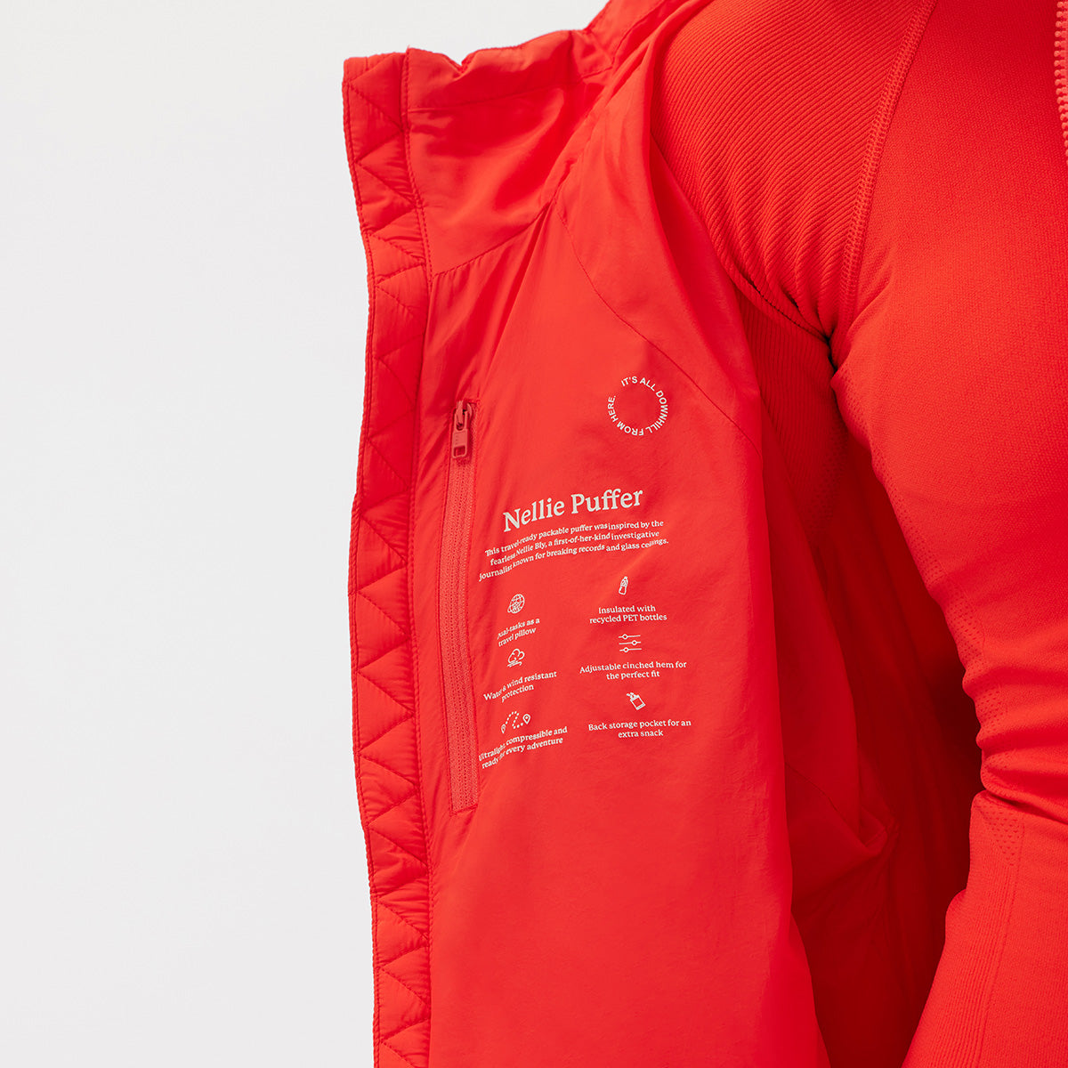 Wearing a bright red Nellie Packable Puffer Jacket by Halfdays, its lightweight quilted design and open side revealing care instructions, a person is ready for an outdoor adventure.