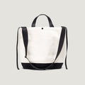 The New York Tote Medium by Bags in Progress boasts a natural upper and black base, complete with black handles and an adjustable shoulder strap. With convenient exterior pockets, this stylish bag offers easy access against a light gray background.