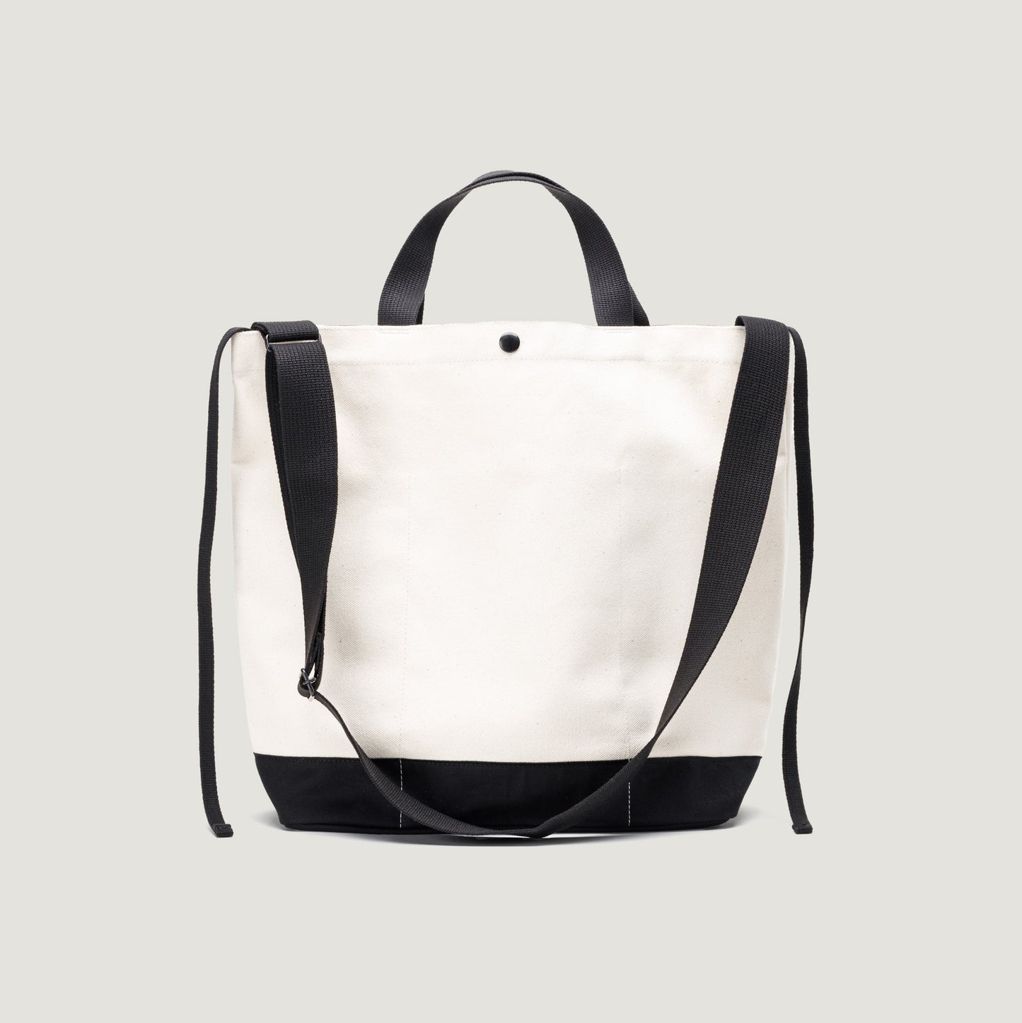 The New York Tote Medium by Bags in Progress boasts a natural upper and black base, complete with black handles and an adjustable shoulder strap. With convenient exterior pockets, this stylish bag offers easy access against a light gray background.