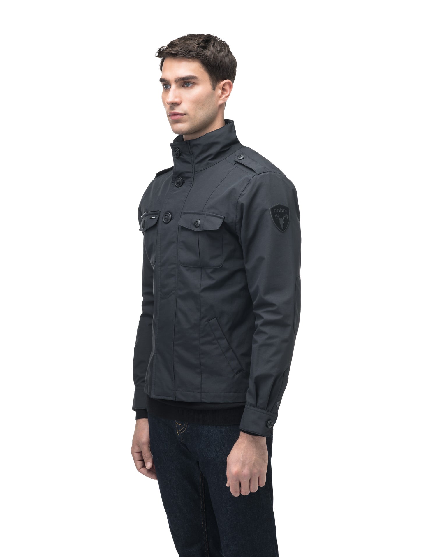 A man wearing the Admiral Men's Jacket by Nobis, featuring advanced fabric technology and buttoned pockets, stands against a white background.