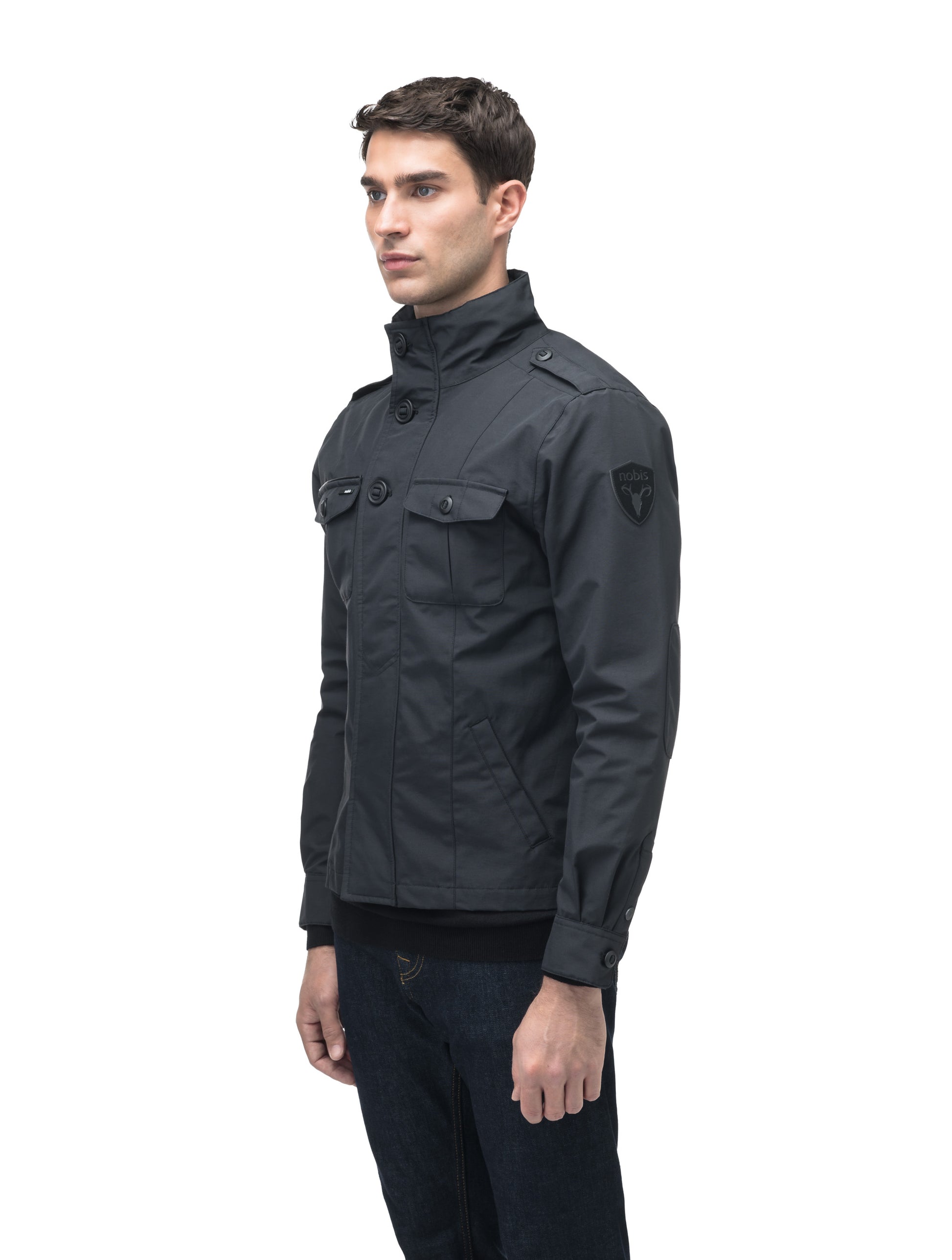 A man wearing the Admiral Men's Jacket by Nobis, featuring advanced fabric technology and buttoned pockets, stands against a white background.