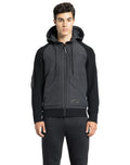 A person wearing a luxurious Hedge Men's Performance Hoodie and dark pants stands against a white background. The hoodie, crafted by Nobis from premium merino wool, effortlessly combines style with water resistance, offering both elegance and practicality.